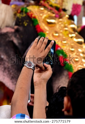 PALAKKAD, KERALA, INDIA, APRIL 03, 2015: What\'s up! A man taking photos using his mobile phone of a decorated caparisoned temple elephant during Nemmara temple festival (Vellangi vela).