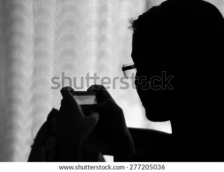 The new generation is addicted to technology. Black and white silhouette image of an Indian teenage girl sending message from her mobile phone.