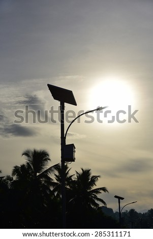 Street light powered by solar energy. Solar panel and LED lamp. Silhouette of a solar street lamps and coconut trees against the setting sun.
