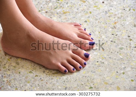 Looking down at the bare feet of a teenager girl. Dark blue nail polish on the toe nails.