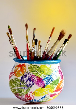Artwork accessories. Paint brushes in a pot decorated by leaf impressions. Brush holder. Artist\'s workshop. stencil art. Colorful leaf impressions on earthen pot.