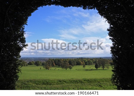 View of the welsh countryside through an archway trimmed into hedge. Wales, UK.