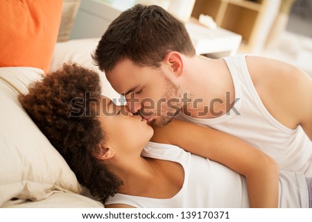 Happy multiethnic couple kissing in bed.