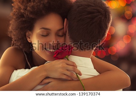 Smiling African woman hugging her boyfriend and holding the rose she got for Valentine\'s Day.
