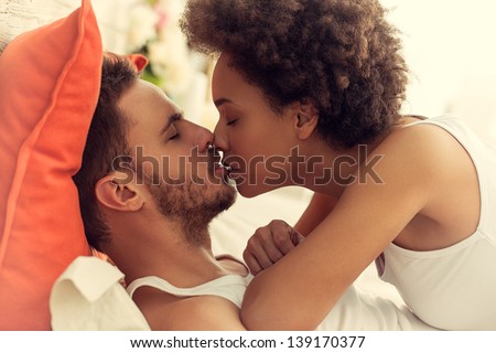 Mixed-Race Couple Kissing In Bed.