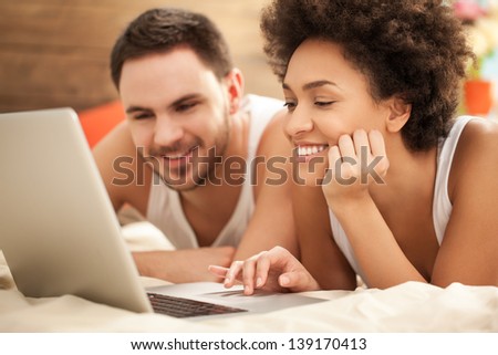 Young mixed-race couple surfing the net together in their bedroom.