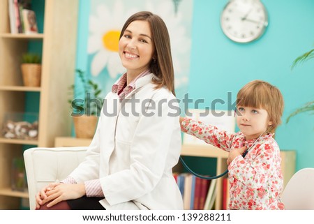 Smiling female doctor and her little patient playing with the stethoscope.