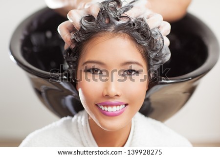 Smiling Asian woman having her hair washed at the hairdresser\'s.