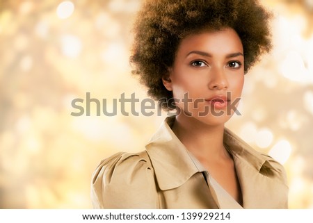 Stylish African-American woman posing in front of a glittering gold background.