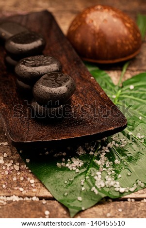 Hot stones used for hot stone therapy with a coconut and a tropical plant leaf.