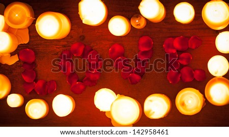 Rose petals forming the word \'love\' surrounded by white candles.