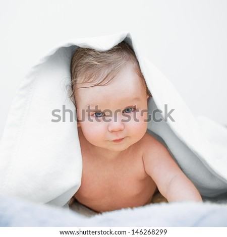 Close-up of adorable baby covered with a white blanket, lying down on bed after bath.