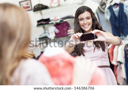 A beautiful young woman taking a photo of her friend at a boutique.