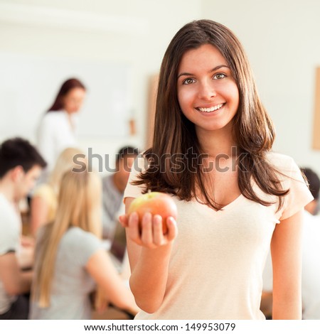 Smiling college student holding an apple and standing in front of her peers.