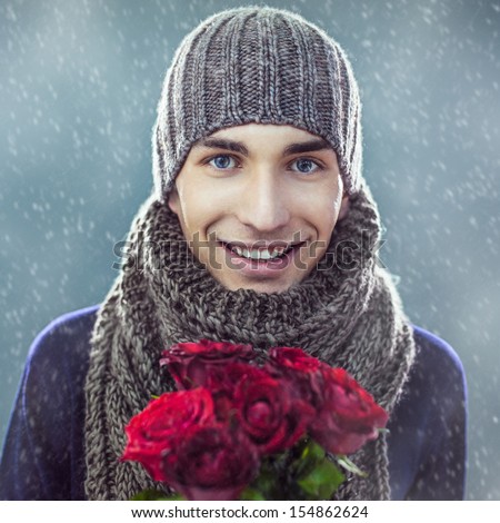 Handsome young man in winter clothes holding a bunch of red roses.