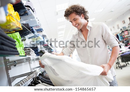 A handsome young man buying a shirt at a boutique.