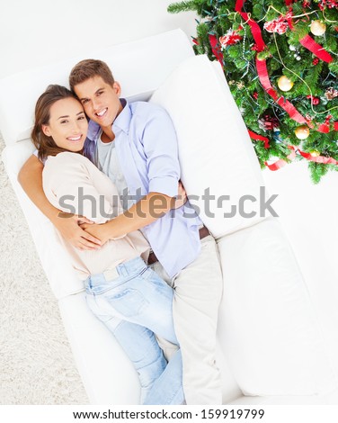 Young couple hugging and lying on their living room sofa on Christmas Day.