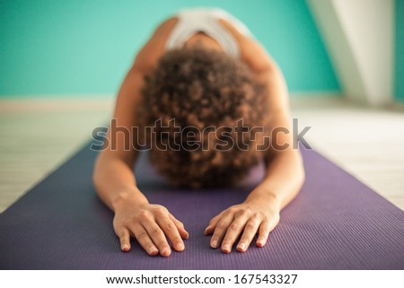 Indoor shot of an African woman doing a forward bend yoga exercise.