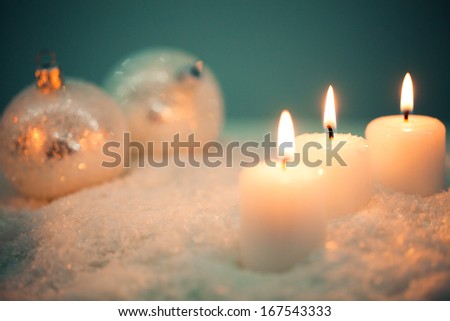 Sparkling white Christmas ornaments and white candles on snow.