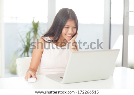 Smiling Asian woman surfing the Internet at home.