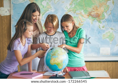 Three students examining a globe with their teacher in a geography lesson.