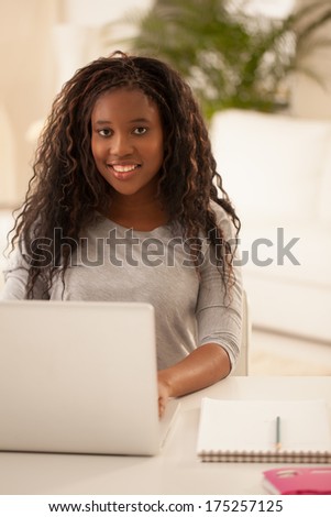 Smiling African teenage girl sitting in her living room with her laptop.