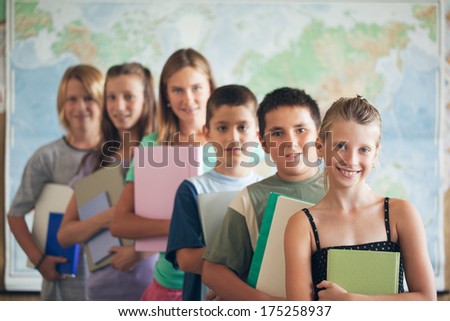 Group of smiling primary school students posing in their classroom in front of a map of the world.
