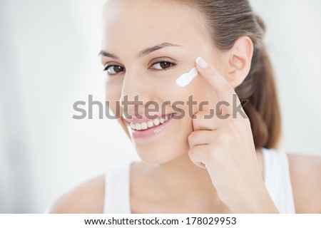 Smiling young woman applying face cream.