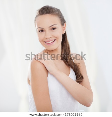 Indoor shot of a smiling young woman touching her shoulder.