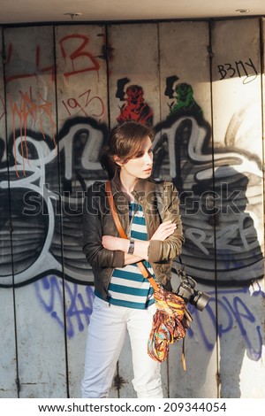 Urban young woman standing by a wall covered in graffiti.