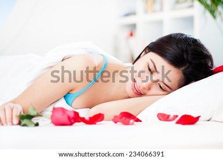 Smiling woman finds a red rose on her bed on Valentine\'s Day morning.
