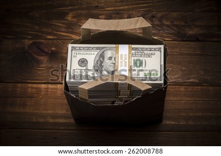 Paper bag full of dollars. Bag full of money - vintage photography including vignetting effect of brown paper bag full of stacks of hundred dollar bills on wooden background