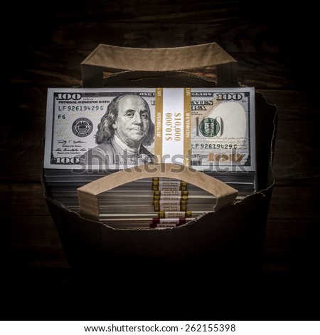 Brown paper bag full of currency. Bag full of money - vintage photography including vignetting effect of brown paper bag full of stacks of hundred dollar bills on wooden background