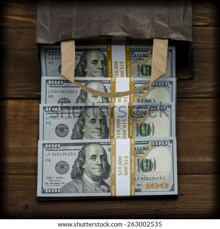 PAPER BAG WITH MONEY. Dollar banknotes coming out of a paper bag on old vintage wooden background
