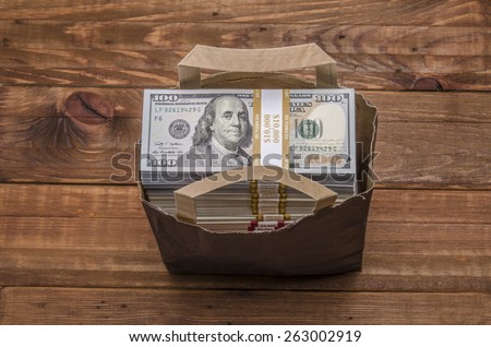 Shopping bag full of currency. Bag full of money - vintage photography of brown paper bag with stacks of hundred dollar bills on wooden background