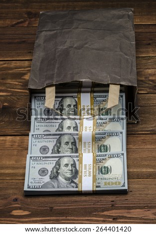 PAPER BAG WITH MONEY. Dollar banknotes coming out of a paper bag on old vintage wooden background