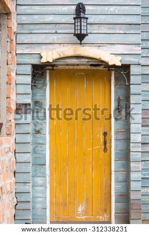 Old yellow wooden door with sign and lamp on blue wall vintage style