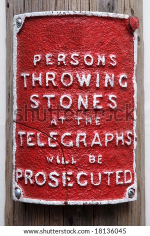 Red sign attached to a telegraph pole warning not to through stones at the pole