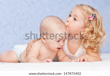 happy little girl hugging kissing his brother on a blue background