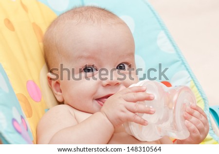 Happy baby holding a bottle and drink water looking at the camera
