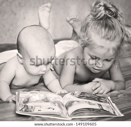 Little Brother And Sister Looking At A Book While Lying On Bed
