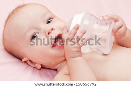 Happy baby holding a bottle and drink water looking at the camera