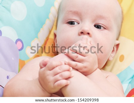 A little baby boy sucking toes on her feet sitting in a chair