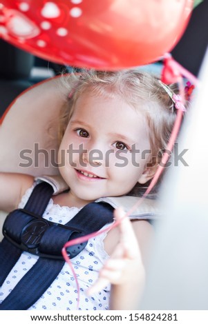 cute toddler girl in car seat  with a red balloon in hand
