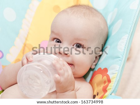 Happy Baby Holding A Bottle And Drink Water Looking At The Camera