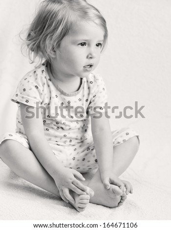 Adorable little girl in pajamas sitting holding hands on their feet ( black and white )