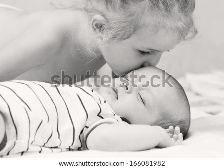 little girl kisses a sleeping baby brother (black and white)