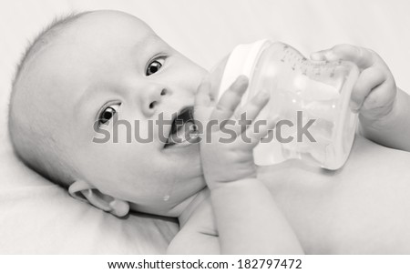 Happy baby holding a bottle and drink water looking at the camera  (black and white)