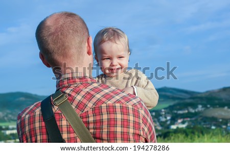 Toddler boy on the shoulder of his father against the backdrop of the mountains