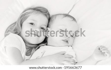 cute little girl hugs a sleeping baby brother on a white background  ( black and white )